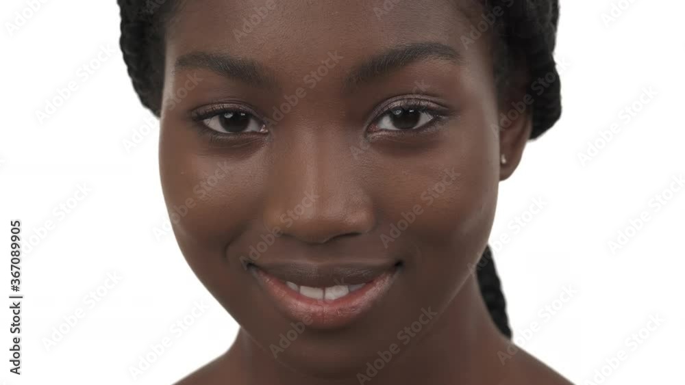 Close-up portrait of young African girl looking at camera and nodding her head with smile. Isolated on white background