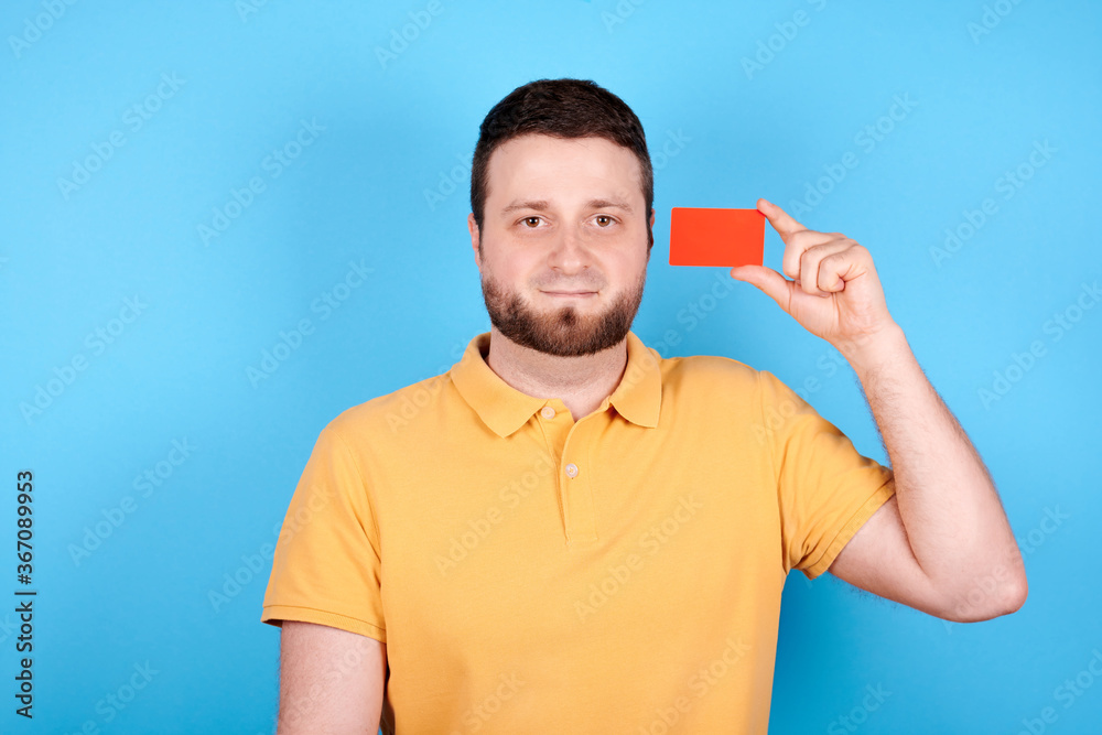 Brunette man holds red credit card in hand. Isolated on blue background. Brunette man holds red credit card in hand. Isolated on blue background.