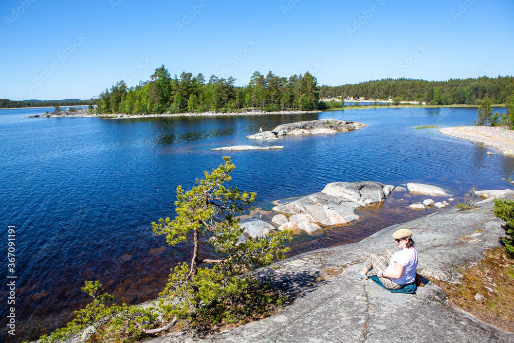 Fototapeta premium A woman on the rocky shore of Koyonsaari Island (southern part) overlooking Erosaari Island. Ladoga lake. Karelia. Russia