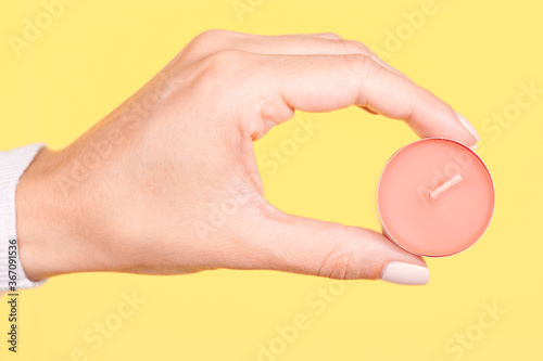 Hand with pink aroma candle. Isolated on yellow background.