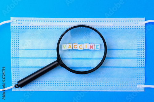 Cubes form the text Vaccine you and a magnifying glass on the background of a medical surgical mask photo