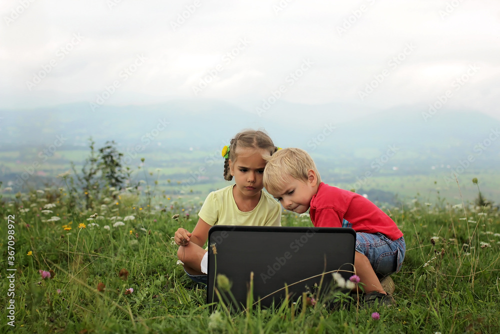 Pupil sitting on green grass outdoor and using laptop for distant studying