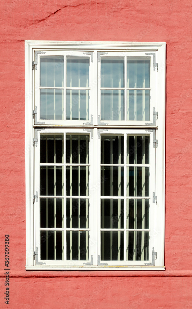 altes, verziertes weisses Fenster an einer roten Hauswand