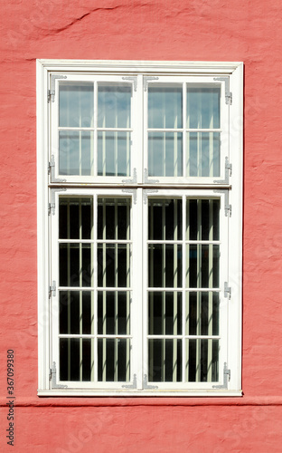 altes, verziertes weisses Fenster an einer roten Hauswand