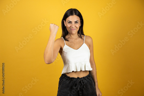 Young beautiful girl over isolated yellow background very proud, celebrating victory and success very excited with raised arm