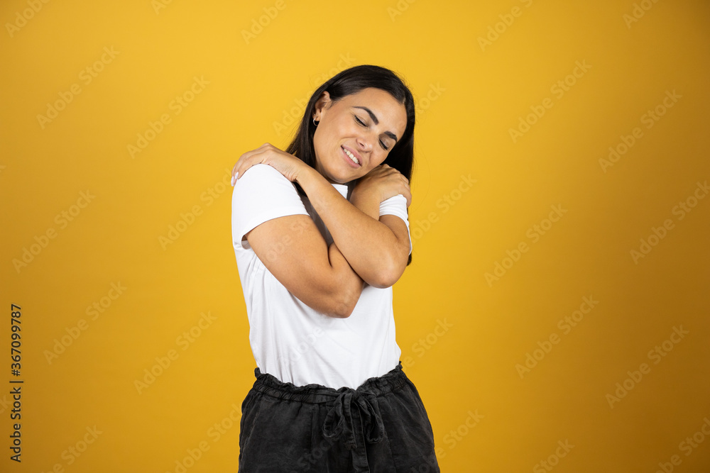 Obraz premium Beautiful young woman on an isolated background hugging herself happy and positive, smiling confident. Self-love and self-care