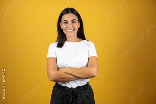 Young beautiful woman standing over yellow isolated background smiling with her arms crossed