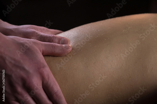 Massagist man scrubbing woman's legs natural scrub in spa salon, hands closeup. Procedure of peeling body of girl in cosmetology clinic. Hands massaging client body. Skincare and bodycare concept.