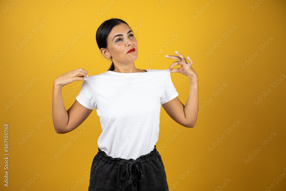 Young beautiful woman with a sucessful expression. Standing over yellow background wearing casual white t-shirt Young beautiful woman with a sucessful expression. Standing over yellow background wearing casual white t-shirt