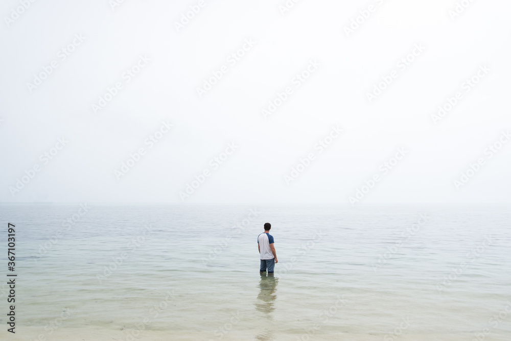 Man stood in water with fog on horizon 