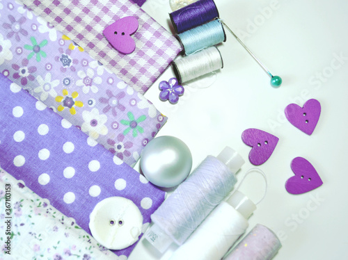Composition of sewing accessories including white-dotted and floral cotton fabrics in lilac and mauve, buttons, sewing spools. Scrapbooking and DIY. Hobby and needle work background.  © Soflet
