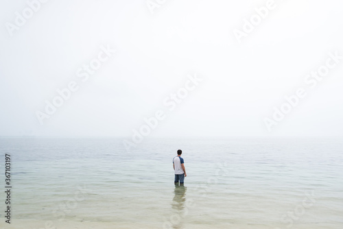 Man stood in water with fog on horizon 