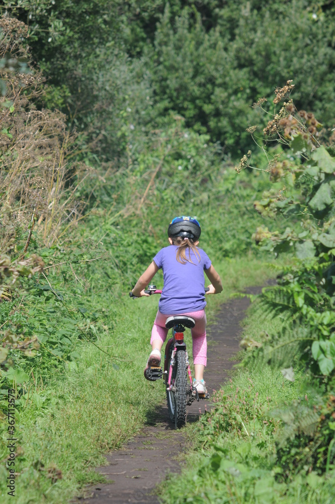 Fototapeta premium Young girl riding a bicycle on a path in the woods