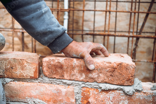 Construction mason, industry worker laying bricks and building walls on construction site. Detail of hand adjusting and placing bricks