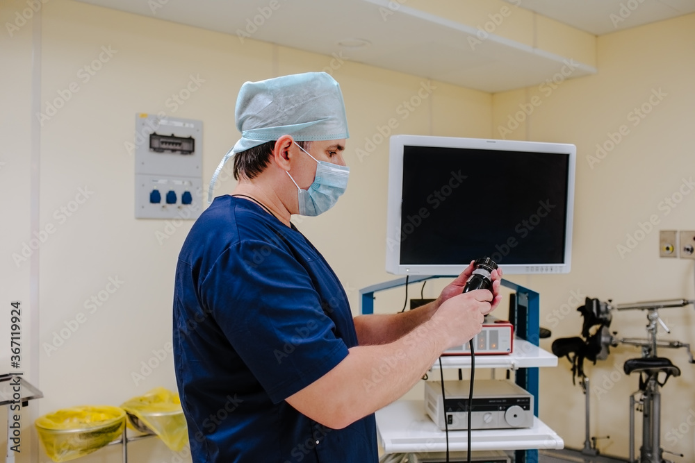 Naklejka premium Adult male doctor at blue medical smock configuring medical equipments at the operation room. Copy space.