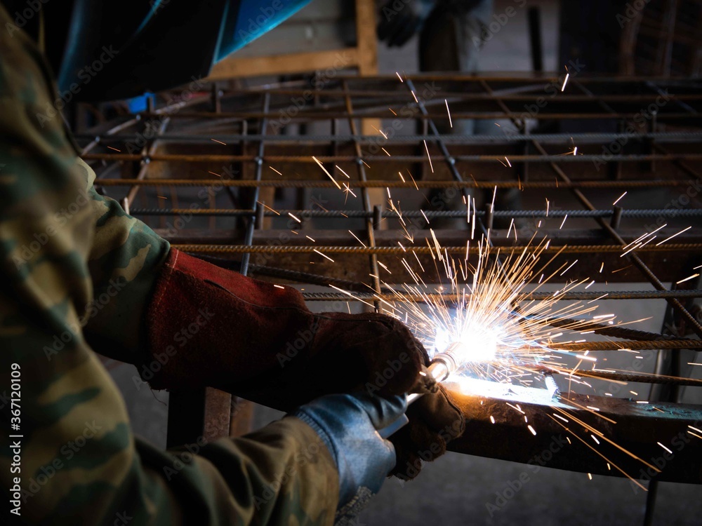 a man in construction clothing is engaged in metal welding. hot sparks fly in different directions. welding