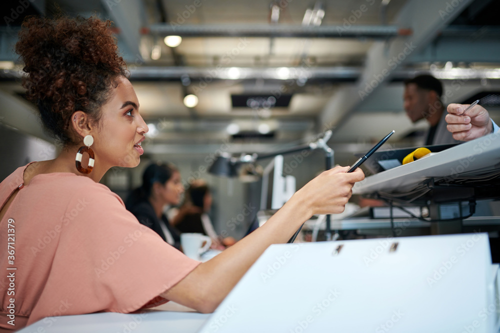Side view of confident businesswoman discussing with colleague while pointing pen at creative office Side view of confident businesswoman discussing with colleague while pointing pen at creative office