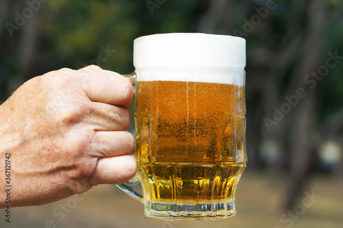 glass mug with beer and foam in a man's hand on the background of nature