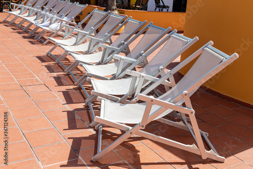 A row of white sun loungers by the swimming pool on a summer sunny day.