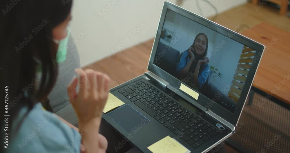 Portrait of young Asian Thai woman chat on laptop, VDO conference on sofa as working at home during corona virus or Covid 19 Portrait of young Asian Thai woman chat on laptop, VDO conference on sofa as working at home during corona virus or Covid 19