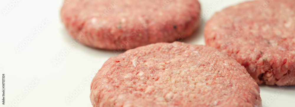 Raw beef burgers with a pinch of salt and black pepper on the white background Raw beef burgers with a pinch of salt and black pepper on the white background