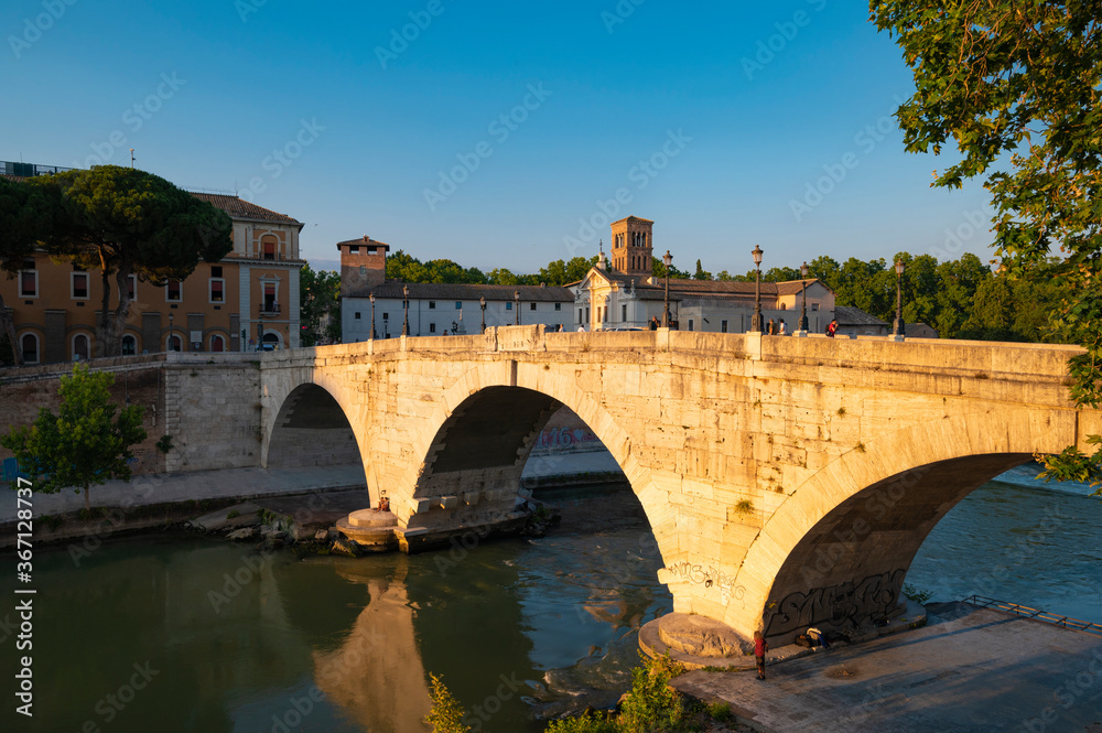 Ponte Fabricio, Rome, connects the Tiber island on the Tiber to the Jewish quarter. View of the arches reflecting in the tiber near the dam on a summer day with blue sky.