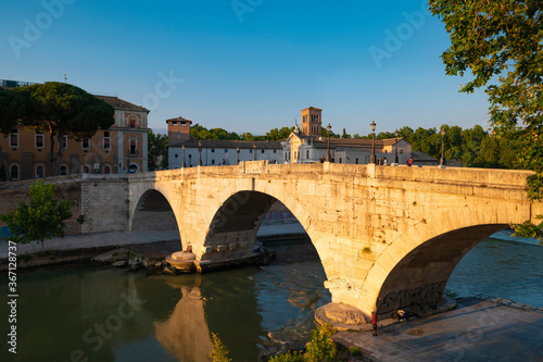 Ponte Fabricio, Rome, connects the Tiber island on the Tiber to the Jewish quarter. View of the arches reflecting in the tiber near the dam on a summer day with blue sky.