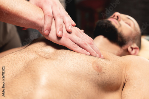 A close-up male masseur does a sports massage of the pectoral muscle to the client athlete in a professional massage salon. The concept of pectoral muscle and breast muscle health