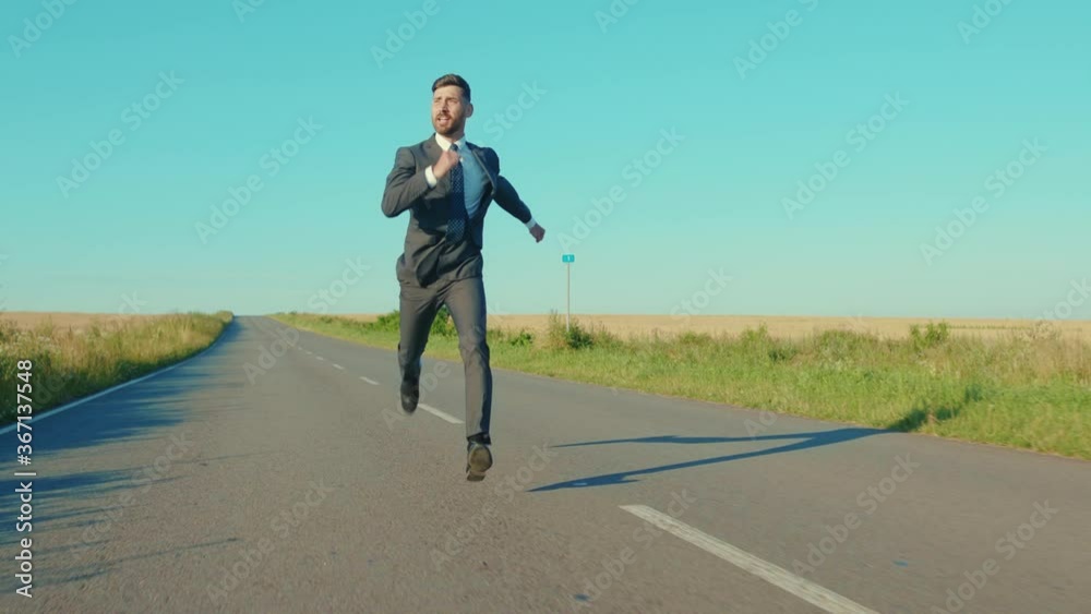 Attractive businessman runs skipping along a country road near a wheat field freedom concept outdoors handsome winner jumping elegant slow motion Attractive businessman runs skipping along a country road near a wheat field freedom concept outdoors handsome winner jumping elegant slow motion
