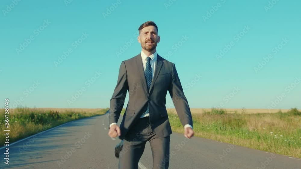 Funny businessman runs skipping along a country road near a wheat field freedom concept outdoors handsome winner jumping elegant slow motion Funny businessman runs skipping along a country road near a wheat field freedom concept outdoors handsome winner jumping elegant slow motion