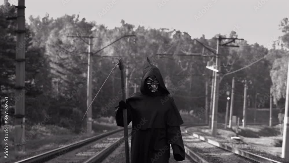 Scary Grim Reaper with Scythe Walking on the Railway Tracks. Slow Motion. Black and White Color Style. Safety for Road Users, Halloween Concept Scary Grim Reaper with Scythe Walking on the Railway Tracks. Slow Motion. Black and White Color Style. Safety for Road Users, Halloween Concept