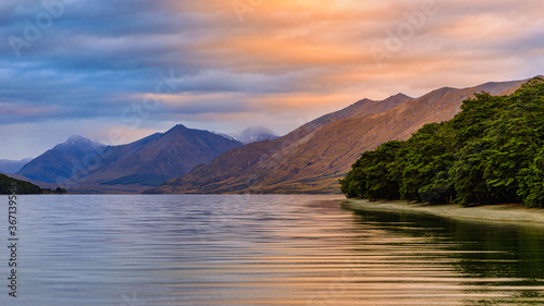 Fotografie North Mavora Lake surrounded by forests with mountains in the background at sunset on a cloudy day