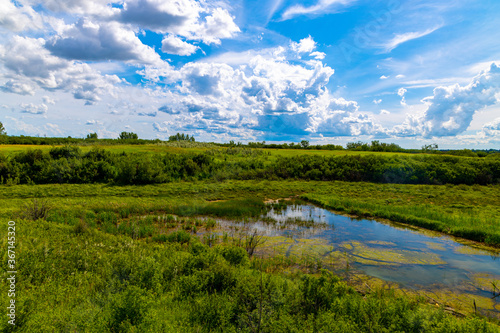 A beautiful wide angle view of a pond hidden at the bottom of a lush valley near Saskatoon Saskatchewan  Canada 