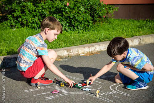 Two brothers sibling kid boy having fun with picture drawing traffic car with chalks. Creative leisure for children outdoors in summer. Difficult traffic rules education friendship concept photo