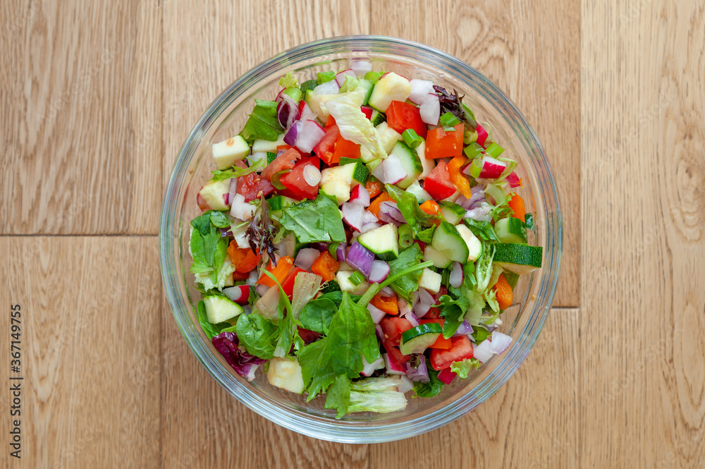 Fresh and healthy vegetables for salad in a glass bowl placed on brown wooden surface. Fresh and healthy vegetables for salad in a glass bowl placed on brown wooden surface.