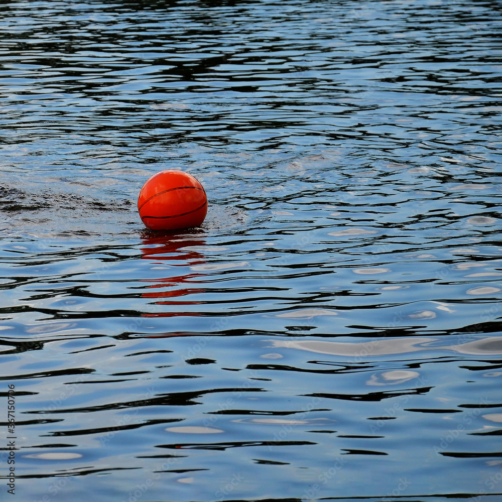 A basketball floats in the lake. Orange ball on the surface of the water.