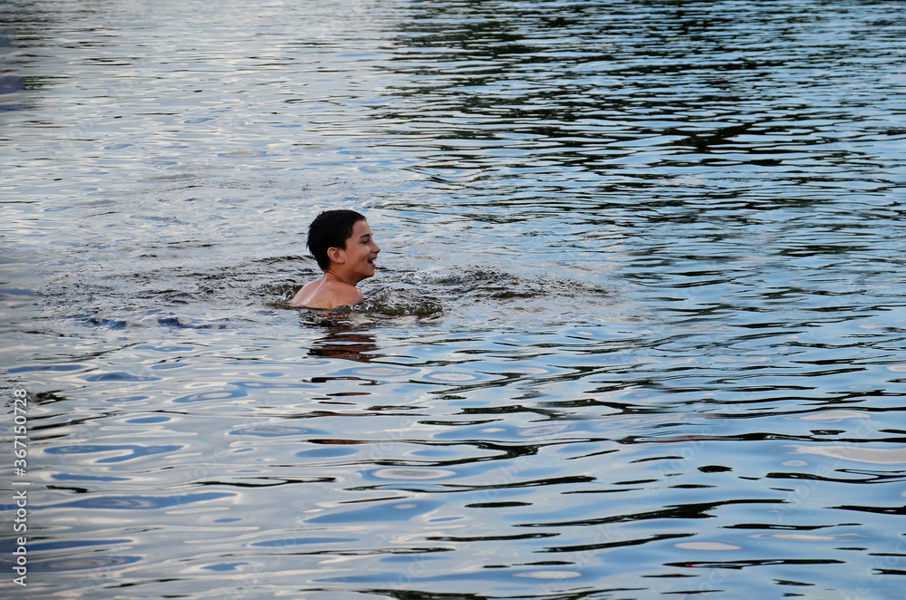 A happy boy is swimming in the lake. A happy child bathes in the sea. Laughing young boy in the water. Recreation, summer, healthy lifestyle.