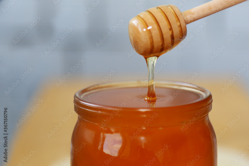 A jar filled to the top with med. Honey drips from a wooden spoon. Sweet food. A stream of liquid honey. Close-up view. A jar filled to the top with med. Honey drips from a wooden spoon. Sweet food. A stream of liquid honey. Close-up view.