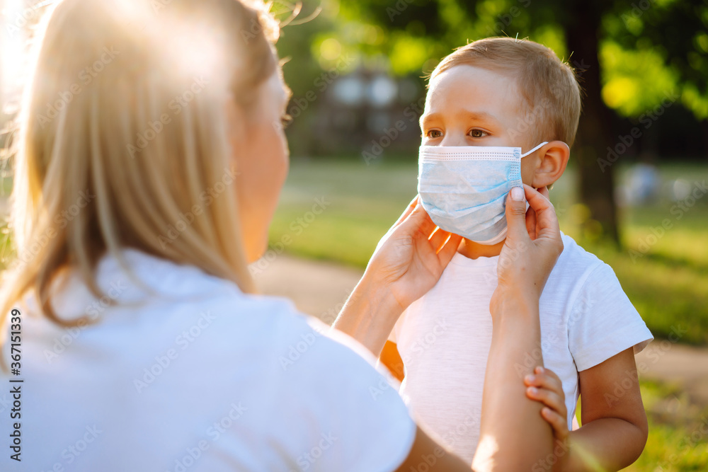 Mother puts on her baby sterile medical mask in the park during pandemic. Covid-2019.
