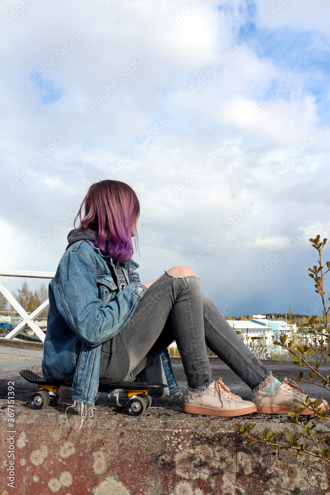Teenager girl with purple hair sits on a skateboard Teenager girl with purple hair sits on a skateboard