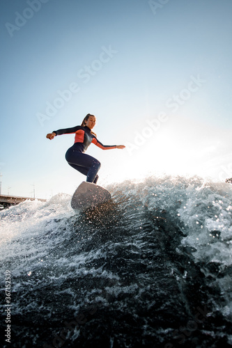young woman in a wetsuit on surfboard rides the wave.