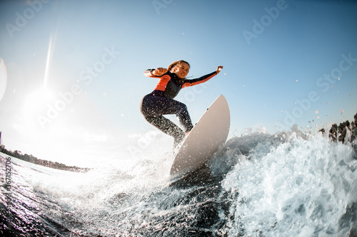 Athletic young woman in wetsuit stands on surfboard and rides on the wave.