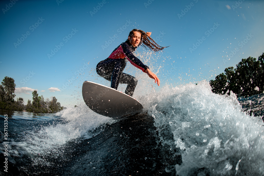 young female sportsman actively rides the splashed wave on surfboard - obrazy, fototapety, plakaty 