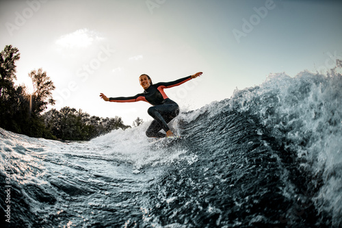 Active young wet woman in wetsuit balanced on surfboard and rides on the wave.