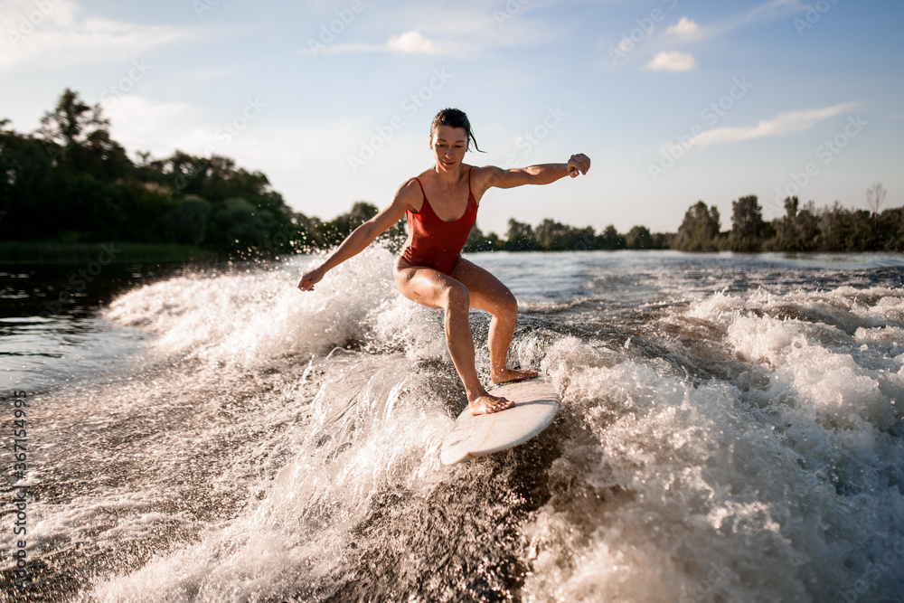 handsome woman rides down on surfboard on river wave from boat