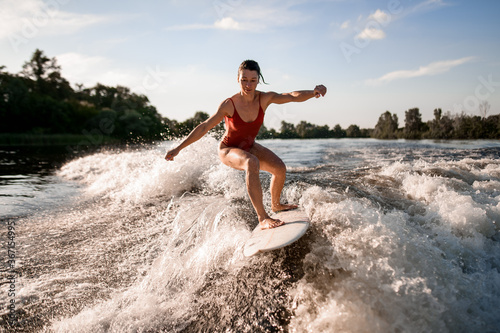 handsome woman rides down on surfboard on river wave from boat