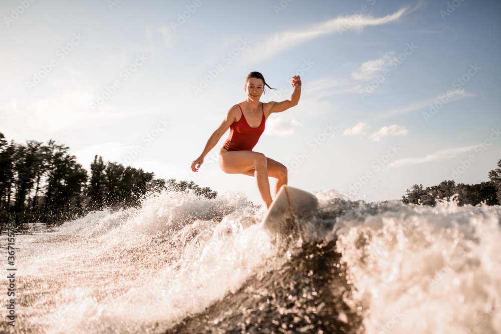 handsome woman effectively rides down on surfboard on river wave