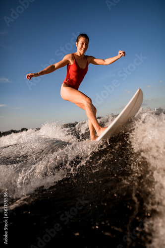 woman wakesurfer in red swimsuit rides up the wave on surfboard