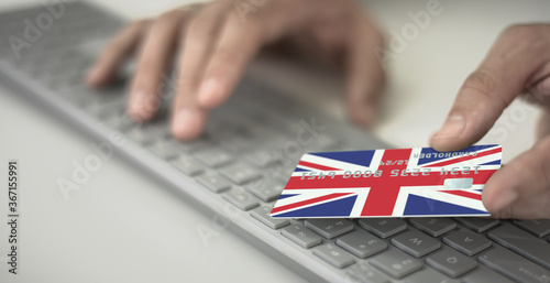 Man pays online with plastic bank card with printed flag of the United Kingdom. Fictional numbers