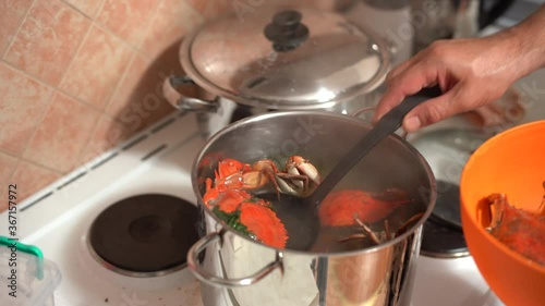 The cook takes out the cooked red blue crabs from the pan and folds them into an orange bowl. photo